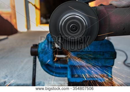 Man With An Angle Grinder Cutting A Piece Of Metal On A Vise