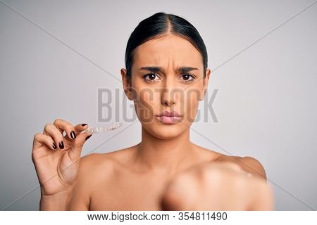 Young beautiful brunette woman holding dental aligner orthodontic to teeth corretion pointing with finger to the camera and to you, hand sign, positive and confident gesture from the front