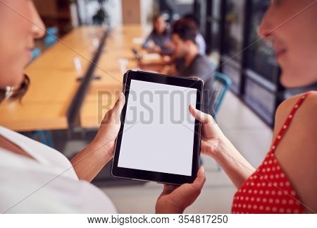 Close Up Of Two Businesswomen Looking At Digital Tablet In Shared Office Workspace