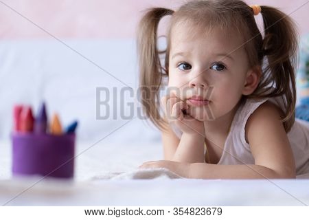 Beautiful Girl Draws With Pencils In Bed. Little Girl Two Years Paints Coloring Book Lying On The Be