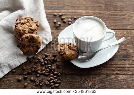 A White Cup Of Cappuccino, Coffee With Froth On A Saucer, Coffee Beans And Cookies Biscuits Nearby. 