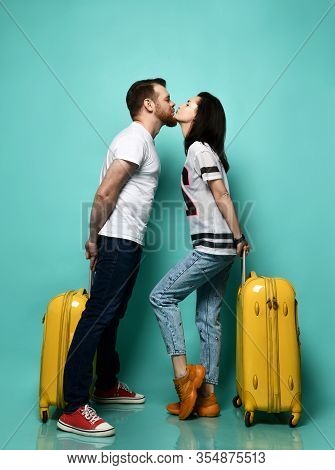 Girl And Guy In Casual Clothes Are Going To Kiss Each Other, Posing With Yellow Suitcases, Standing 
