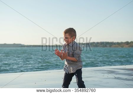 Funny Happy Active Little Kid Applause With Joy Playing On Sea Coast In Port City In Spring Storm We
