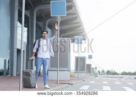 Catching A Cab. Male Traveller Standing Near Airport, Waving Hand, Calling Taxi Driver, Free Space