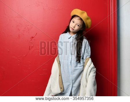 Nice Cute Asian Kid Girl Iblue Shirtdress Felt Beret And Beige Jacket Is Posing Over Red Background