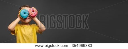 Happy cute boy is having fun played with donuts on black background wall. Bright photo of a boy. Colored donuts. Panorama