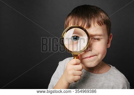 Child see through magnifying glass on the black backgrounds. Big kid eye