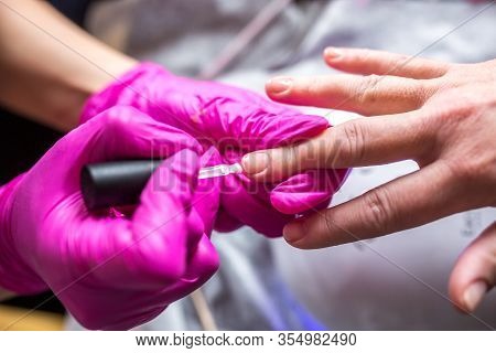 Manicure Master In Pink Gloves Scraping Off The Old Coat Of Varnish In Manicure Salon Using Drill.