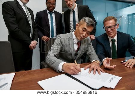 Confident Asian Businessman Signing Some Document While Having A Meeting With His Business Partners 
