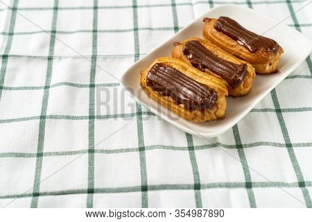 Custard Cakes With Chocolate Icing On A Tablecloth Cage Background. Copy Space