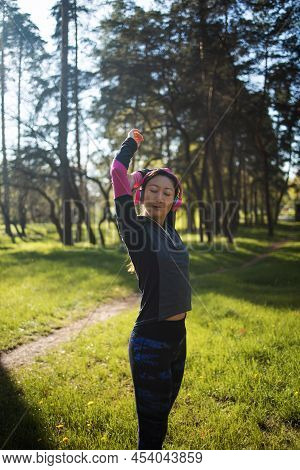 Pretty Young Asian Woman With Pink Earphones Preading Her Arms In The Forest Because She Enjoys Trai