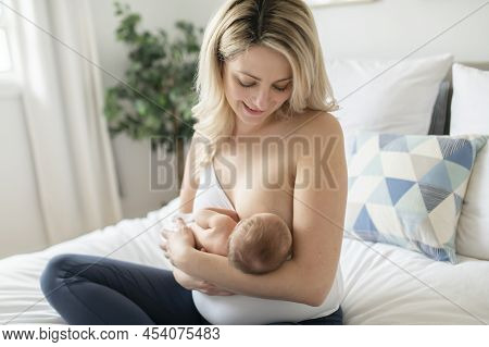 Woman In Her Bedroom On The White Cushions, Smiling And Breastfeed Her Baby.