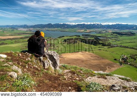 Couple Sitting On Top Of The Hill And Looking On Beautiful Nature. Spring Country Landscape At Slova