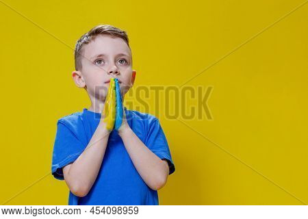 Ukrainian Boy Prays For Ukraine. Children Against War. A Boy In A Blue T-shirt On A Yellow Backgroun