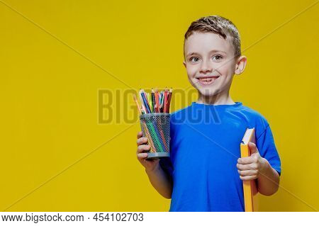 Smiling Happy Schooler In Blue T-shirt Holding Multicolored Pencils And Book On Yellow Background