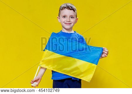 Little Boy Smiling Holding A Yellow And Blue Flag, The Flag Of Ukraine. The Kid Will Support Ukraine