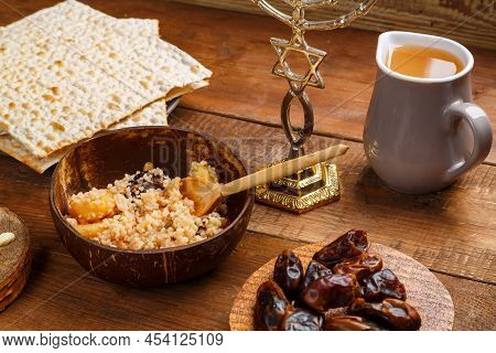 A Plate Of Couscous With Fruits And Nuts On A Wooden Table Next To Matzah And A Jug Of Fruit Broth. 