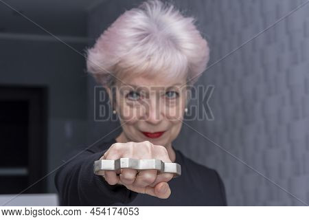 An Elderly Woman Strikes With Brass Knuckles On A Light Background, Close-up, Selective Focus. Conce