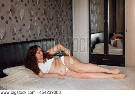 Curly Plus Size Woman In White Underwear Lying On Bed In Bedroom And Massage Thick Hips With Body Br