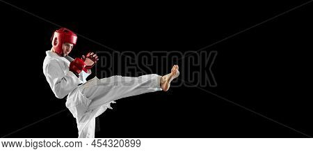 Male Taekwondo Fighter In White Dobok, Helmet And Gloves Training Isolated Over Dark Background. Con
