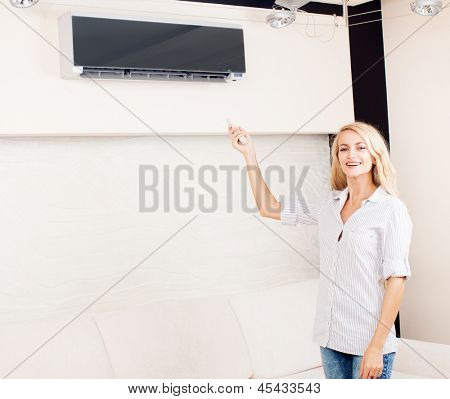 Femme tenant un climatiseur télécommande à la maison. Heureuse jeune femme sur canapé