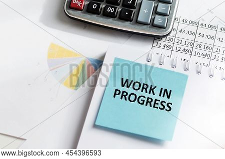 A Card With The Text Work In Progress Text Pasted On A Notebook On The Office Table Next To It Lies 