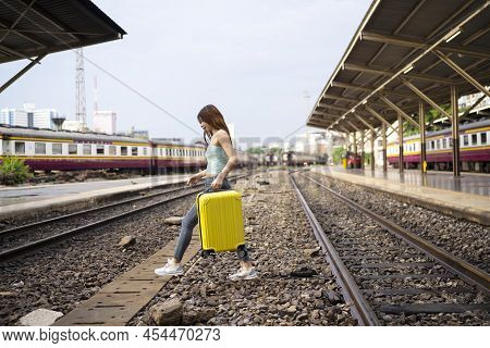 An Elegant Woman With A Suitcase Traveling By Rail Autumn Day. Travel Across The Railroad To Get On 