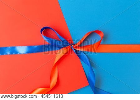 Red And Blue Ribbon Tied In A Bow On A Red And Blue Background. The Concept Of Union, Unification, H