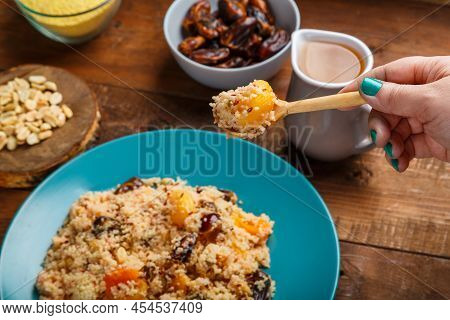 A Plate Of Couscous With Dried Fruits And Nuts On A Wooden Table With A Wooden Spoon. Horizontal Pho
