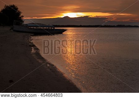 Bright Majestic Golden Sunset On Ocean With Dark Silhouette Volcano, Boat On Shore, Black Coastline,