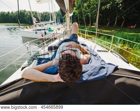 Adult Man Laying On A Sailboat Deck And Taking Sunbath During His Vacations In A Sunny Summer Day. Y