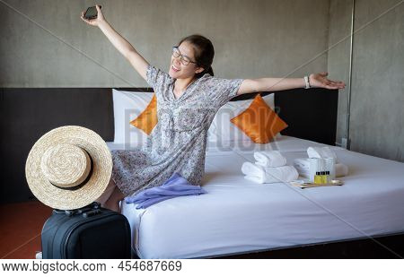 Happiness Asian Tourist Woman Sitting On Bed After Check-in In Hotel Room. Conceptual Of Woman Lifes