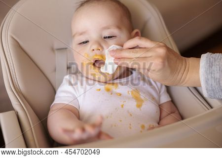 Mother Wiping Baby Using Wet Wipes After A Meal, Introducing First Solid Food Meal, Baby Sitting In 