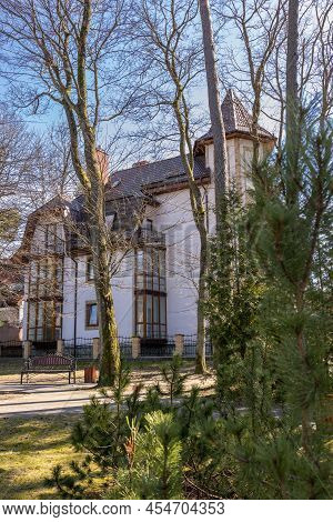 A Low Beautiful Modern House Is Located Behind Green Fir Trees In Spring In Sunny Weather In Svetlog