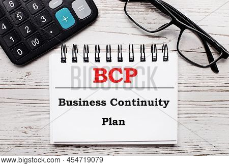 On A Light Wooden Table Calculator, Glasses And A Blank Notepad With The Text Bcp Business Continuit