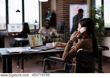 Business Woman With Health Condition Answering Landline Phone Call In Disability Friendly Office. Us