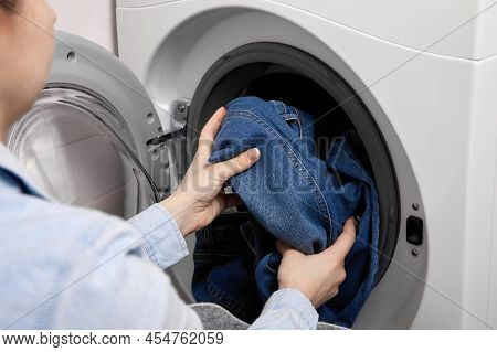 In Laundry Room, Female Person Loads Dirty Laundry Items Into The Washing Machine. Woman In Light-co