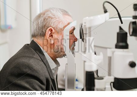 Examines Elderly Mans Eye On Screen Of Autorefractometer.