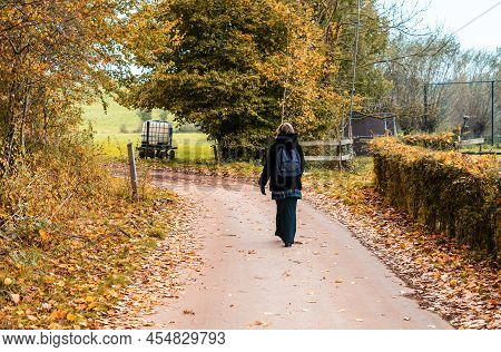 Attractive Thirty Year Old Woman  In A Black Furry Coat Walking Away On A Trail In An Autumn Forest,