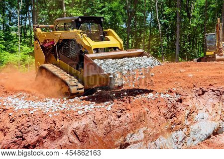 Skid-steer Loader Mini Excavator Unloading Gravel At Construction Worksite Outdoors