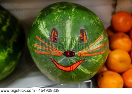 Common Green Watermelon (latin Citrúllus Lanátus) With A Painted Muzzle On A Background Of Oranges. 