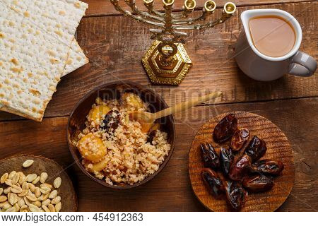 A Plate Of Couscous With Fruits And Nuts On A Wooden Table Next To Matzah And A Jug Of Fruit Broth. 