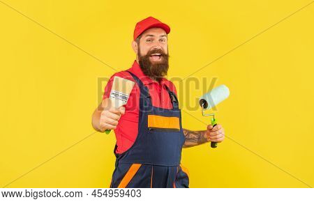 Cheerful Bearded Man Housepainter In Work Clothes Hold Paint Roller And Brush
