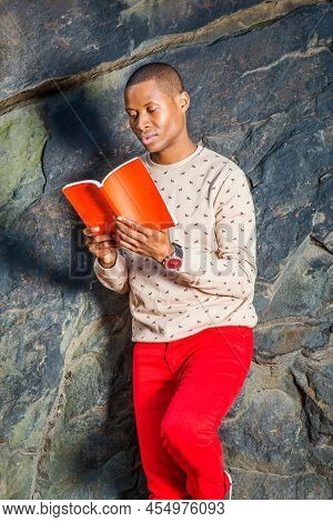 Man Reading Outside. Dressing In Cream, Patterned, Collarless Sweater, Red Jeans, Wearing Wristwatch