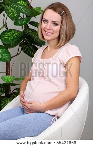 Young regnant woman sitting on armchair at home