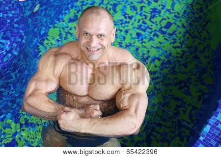 Top view of happy middle-aged bodybuilder standing in swimming pool 