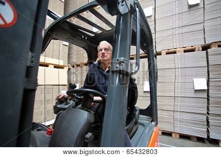 Forklift driver inside a forklift, manipulating a joystick in a warehouse full of pallets empty, plano, cardboard boxes