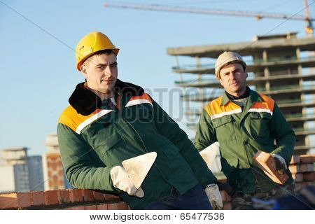 two construction mason worker bricklayer installing red brick with trowel putty knife outdoors
