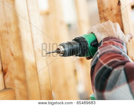 Closeup of a carpenter's hands using a drill on a construction site.  Focus on drill and hand.  Shallow depth of field.