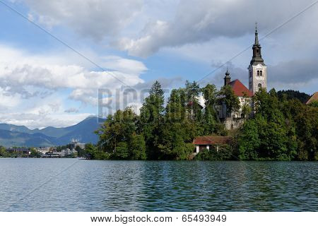 Church on an island on Bled lake with mountains and resort on the background